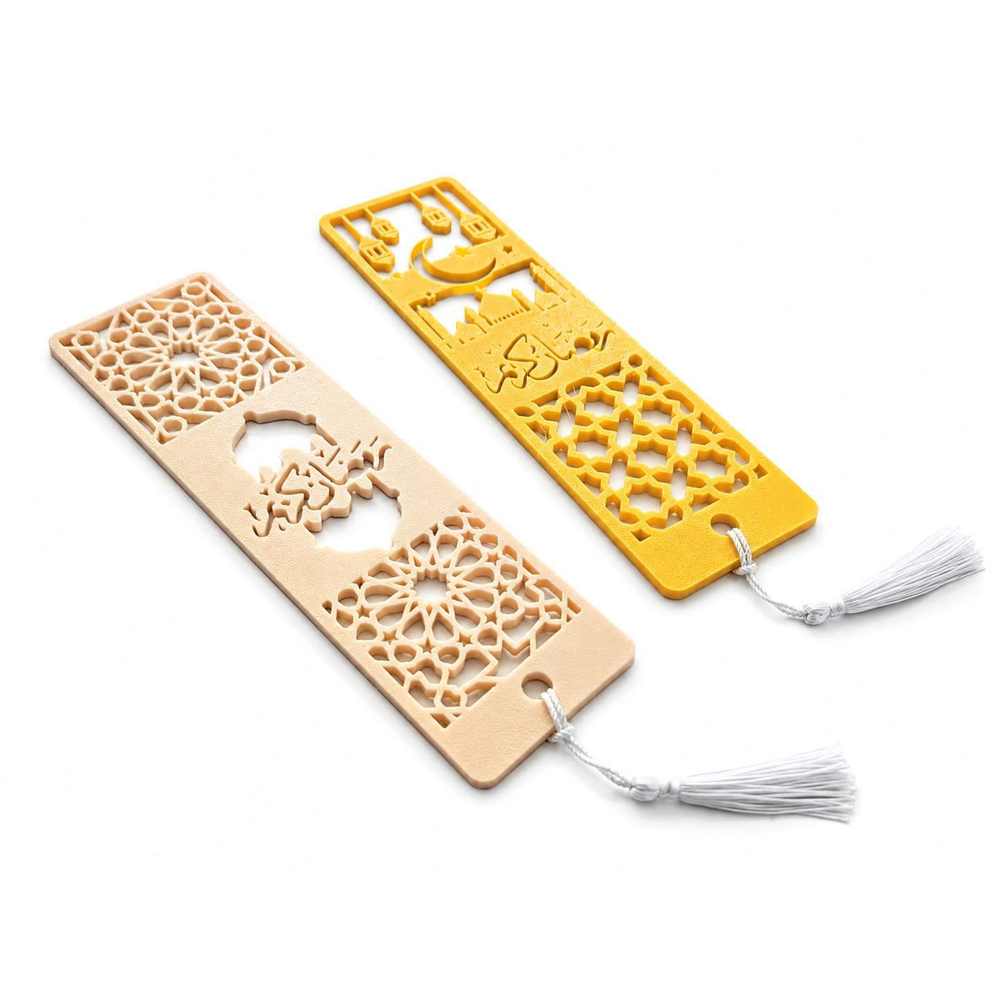 Two 3D printed bookmarks, one cream and one yellow, with Arabic lettering, a mosque skyline and lantern shapes, each tied with a white tassel.