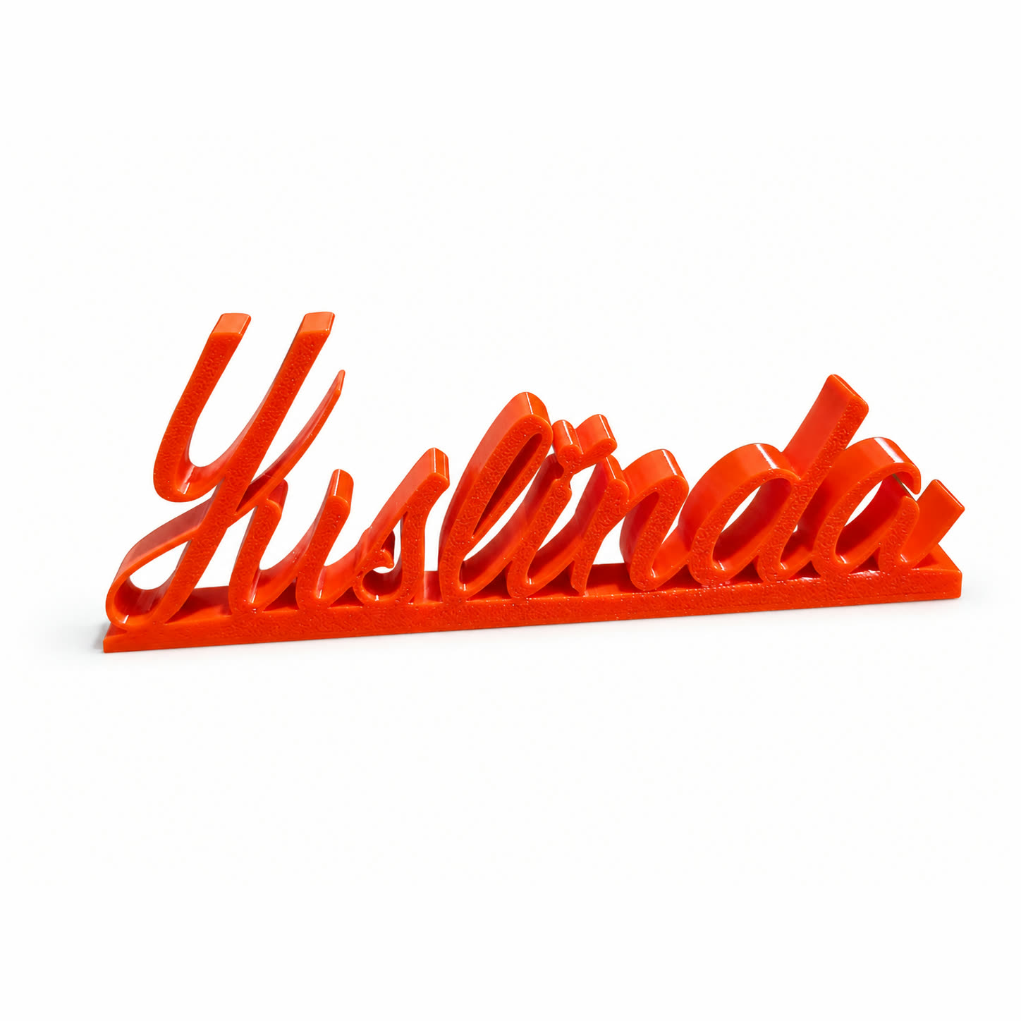 An orange 3D printed name, Yuslinda, in joined-up script standing upright on a thin base.